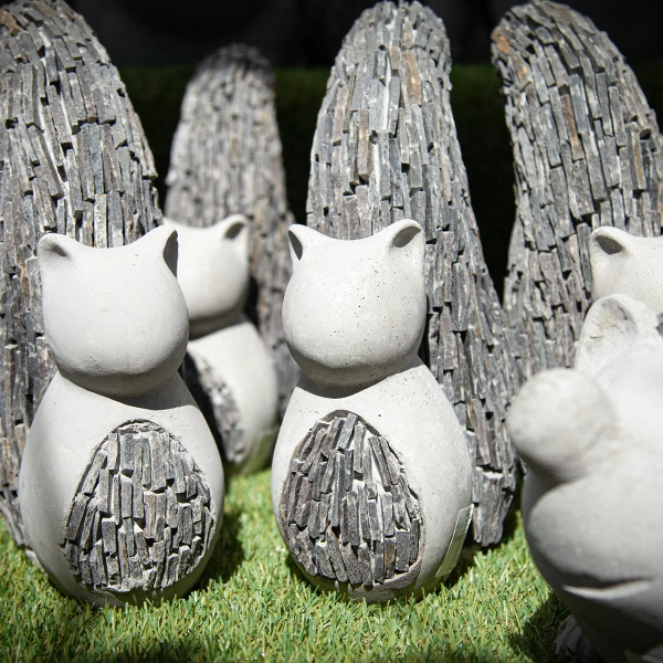Sculptures d'ecureuilles en céramique avec des motifs en forme d'écailles de poisson, disposées sur une surface herbeuse. Les sculptures sont de couleur blanche et ont des détails texturés.